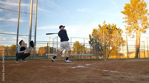A young baseball player hits a pop fly ball and then ducks to avoid getting hit on the head in slow motion over home plate.