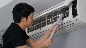 Young man using vacuum cleaner to cleaning the air conditioner at home Stock Video
