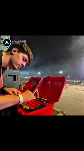 axisrnx18M on Instagram: "This video provides a rare, behind-the-scenes perspective of a pyrotechnician operating a control console during a live concert event. The technician is shown intensely focused, wearing in-ear monitors to stay synced with the music while manually pressing buttons on a specialized red launch briefcase. As he strikes the controls in rhythm with the song's beat, various pyrotechnic effects including Roman candles and vertical spark fountains ignite on stage and in the back