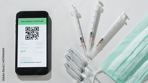 Electronic vaccination passport on phone close-up, covid 19 vaccine qr code on smartphone. Medical protective mask and syringes with ampules on table.