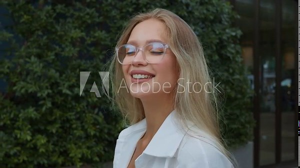 Stunning blonde lady in glasses stands on street gazing into camera with captivating smile close-up shot. Enchantingly beautiful blonde woman with glasses stands outdoors smiling at camera.