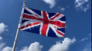 Union Jack British flag flying against a bright blue sky with a few white clouds, on a windy day