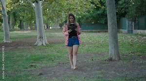 young brunette Caucasian girl walking barefoot through the grass with her back to the camera reading a book
