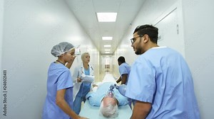 Following dolly shot of female doctor giving instructions to multi-ethnic group of nurses pushing gurney and administering oxygen and IV fluids to unresponsive elderly patient while rushing him to ER