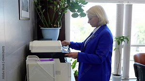 Caucasian female in office makes photocopies of documents using copier engaged in paperwork. Office woman worker uses copy machine to duplicate documents and papers technology in tasks.