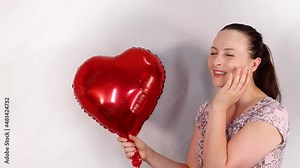 An attractive young female model wearing a cute flowery dress, with the woman holding up a balloon in the shape of a love heart looking happy and excited.