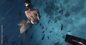 Attractive woman freediver swim with large Sting ray fish in blue ocean in the Maldives.