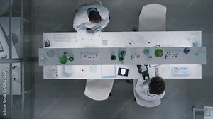 Top view of couple scientists working together at table with microscope and samples in test tubes in laboratory