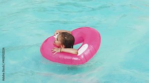 A child happily floats in a pink inflatable ring in the pool. An ideal choice for advertising children's products, summer vacations, and water fun.