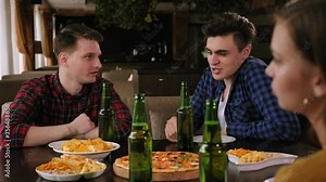 Friends relax in a restaurant, they drink beer, eat chips and pizza and have fun talking. Two men are talking in a bar, young girls are sitting nearby.