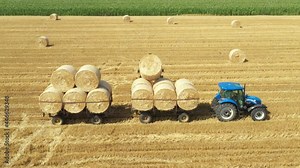 Above view on excavator as loading straw bales on trailer, tow by tractor at farmland, using forklift blade, additional carrier. Stock Video
