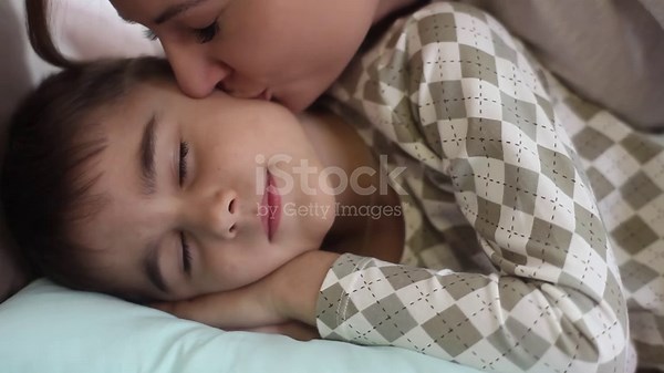 Maman baise son fils bien-aimé pendant qu’il dort sur le lit et les...