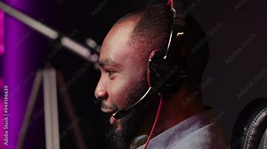 Close up of gamer having fun by competing in online multiplayer videogame, using headset mic. Man laughing while playing on gaming PC, talking with mates through headphones microphone, camera A