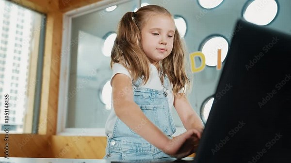 Cute girl using laptop programing software while looking at camera with confident to celebrate successful project. Pretty child coding system while smiling at camera proudly in Stem class. Erudition.