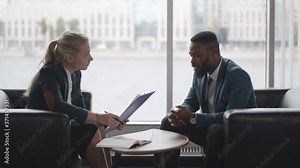 Young HR woman interviews afro-american male candidate for job sitting on couch in conference room