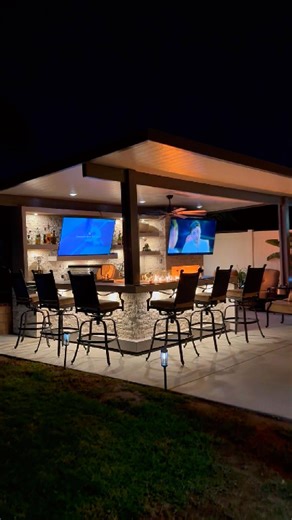 BBQ Islands & Designs on Instagram: "This is where nights are meant to be spent. A complete outdoor living space designed for long evenings, good conversation, and effortless hosting, all under one patio cover. A custom fireplace with an 85” TV anchors the space, flanked by built-in shelving and a dedicated seating area that comfortably seats 5, perfect for unwinding once the food is on the grill. The media wall keeps guests engaged with its own 85” TV, bar center, shelving, stainless steel stor