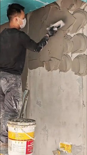 using a metal trowel to apply and spread thick grey plaster over a vertical concrete wall surface