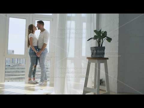 Young happy couple embracing ang kissing near window in their new apartment
