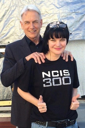 "300 Episodes of NCIS – A Legendary Milestone!" A cheerful behind-the-scenes moment featuring two iconic NCIS stars. The woman in the front proudly wears a black T-shirt with the bold print "NCIS 300", celebrating the show’s 300th episode milestone. She gives two thumbs up with a big smile, while the man behind her places his hands on her shoulders, smiling warmly. The backdrop suggests a casual on-set environment, highlighting the excitement of this major TV achievement. #NCIS300 #NCIS #300Epis