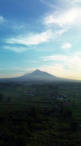 4k aerial footage of Mount Merapi at a distance of about 12 miles. Panoramic portrait of an active volcano from a distance after sunrise with rice fields and settlements in the foreground