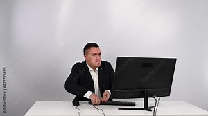 Caucasian man in a suit gets angry and smashes the keyboard on the monitor. An office worker in a rage breaks the computer.