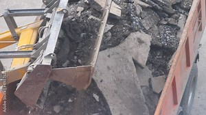 An excavator loads broken stones and soil into a dump truck at a construction site. Large construction equipment and transport. Excavator bucket loading body at construction site