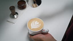 Hands making latte art in coffeeshop close up. Barista pouring milk...