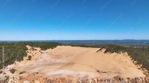 Aerial flies across Rainbow Beach's famed Carlo Sand Blow nestled within the rich forest of the Great Sandy National Park. Clear fine and calm day at the Fraser Coast Queensland Australia.