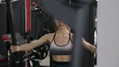 Beautiful young woman trains pectoral muscles on the simulator