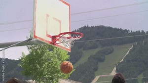 basketball swish through net flapping after exit, small town community court with mountain backdrop, tripod lockoff low angle, slow motion