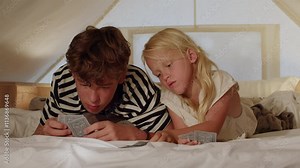 Siblings enjoying a card game on a bed, sharing laughter and moments of concentration in a cozy indoor setting