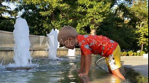 Child have fun near city fountain on summer day. Little boy wearing sun protection shirt playing with water. Catherine Park, Simferopol, Crimea, Russia 2024.
