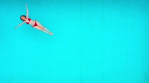 View from the top as a woman in red swimsuit lying on her back in the pool. Relaxing concept