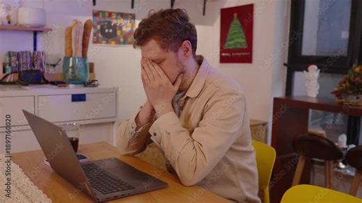 Exhausted young professional feeling overwhelmed and stressed while working late on laptop, rubbing his tired eyes and temples in his home office due to burnout and work related problems