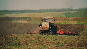 Agricultural tractor sowing and cultivating field. Tractor with a plow trailer plowing the field after sunset.
