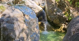 Small turquoise waterfall with crystal clear green pond in Samaria Gorge, Crete, Greece, large white boulders around.