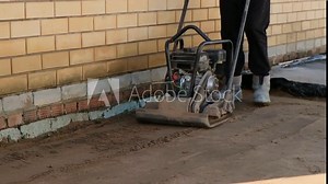 Worker using vibrating soil compactor for sand ramming. Construction and renovation.