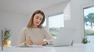 Happy middle aged woman using laptop computer sitting at home table elearning. Smiling older mature lady hybrid working, learning with device at home, typing, browsing writing notes in living room. Stock Video