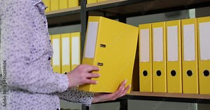 Employee takes folder with accounting materials for paperwork. Woman take yellow folder shelf