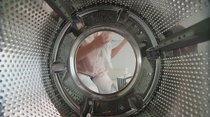 Premium stock video - Woman puts white linen inside washing machine 1