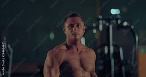Bodybuilder shows body muscles in front of a mirror in the gym. Handsome male athlete with big chest muscles. Portrait view.