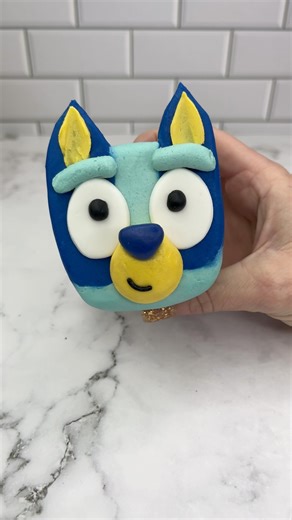 BLUEY 💙🩵 (did you know that Bluey is a girl?) Turning a cupcake into Bluey 💙🩵💙 I used buttercream to attach Oreo halves to the top of the cupcake. I then used a large round piping tip to add two shades of blue buttercream on top. 🩵 I pressed it onto parchment paper and froze it for 20 minutes. 💙 I used a palette knife to add some yellow buttercream for the ears.🩵 The eyes and nose are made from fondant. 💙 I added his eye brows using tip 12 and the yellow face using Ateco tip 809. #cupca