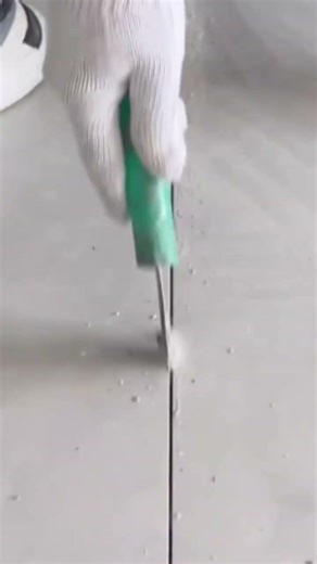 Cleaning ceramic floor tile grout lines using a small metal scraper for a neat renovation finish