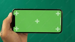Horizontal smartphone in the hand closeup isolated at green background. Phone screen is green chroma key, background with another chroma key green screen. Footage for mobile ads, app promo.
