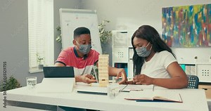 Break in the office from work, two young interns are building tower of wooden blocks at the desk, from behind comes disgruntled boss in maroon suit, spoils fun for employees by smashing building