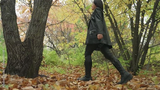 full body woman walking through woods with confident stride side profile of leatherclad walker moving along leafstrewn trail, autumn tones, steady pace, cinematic framing suggesting journey