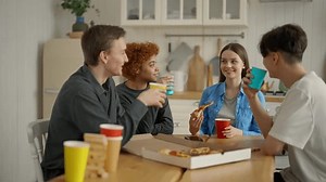 Guy telling interesting funny story sitting at home kitchen with colleagues or friends enjoy time together. Company listen and laugh, smile. Young best friends enjoying party eating pizza drinking.