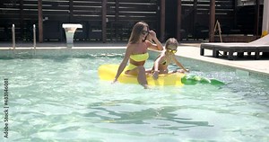 Mother and daughter with inflatable pineapple mattress in swimming pool