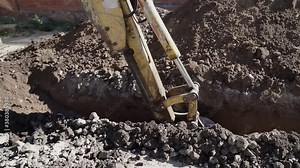 Big metal excavator bucket scoops up dirt while digging a ditch during roadworks in countryside. Ripper bucket excavating soil and rocks at a construction site on a sunny day.