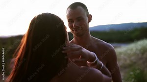 Attractive woman takes off her shirt and kisses a boy as the sun sets. Medium shot.